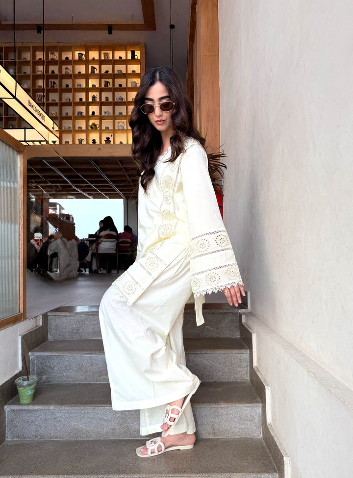 Woman in a white outfit sitting on a staircase in an indoor setting.